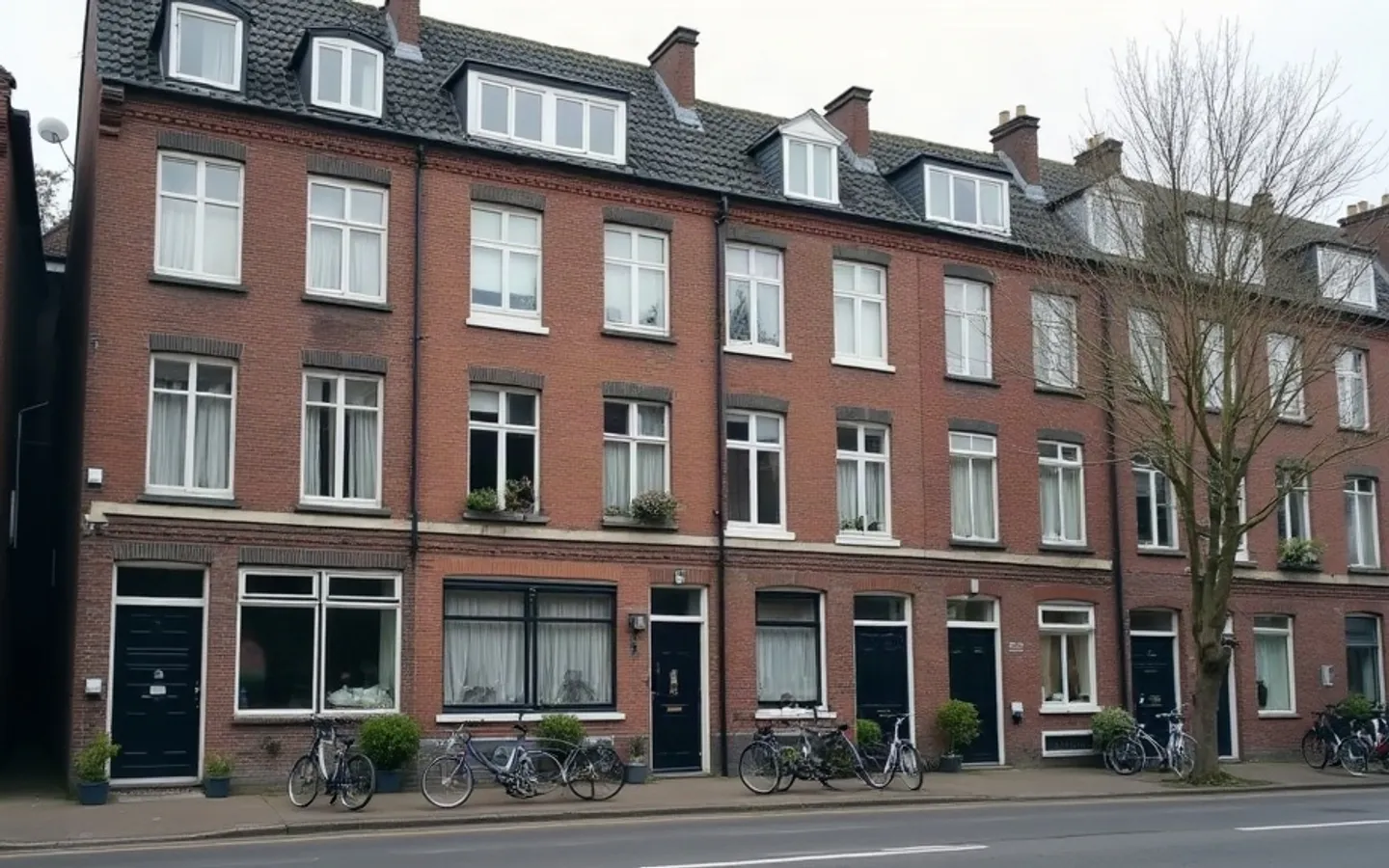 Rij Nederlandse bakstenen appartementengebouwen aan een stille stadsstraat in ochtendlicht, met fietsen bij de entrees.